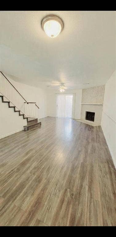Open-concept area featuring wood-finish flooring, a corner fireplace with a stone-surround hearth and mantel, a staircase with metal railings, and glass sliding doors