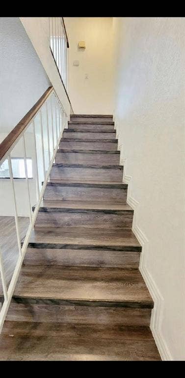 Staircase featuring wood-finish treads, a white metal railing with a stained wood handrail, and applied wall molding