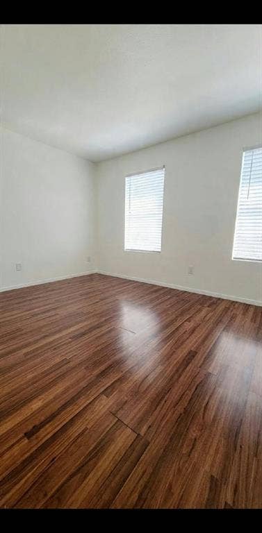 Interior space featuring wood-finish flooring, neutral walls, and dual windows with horizontal blinds