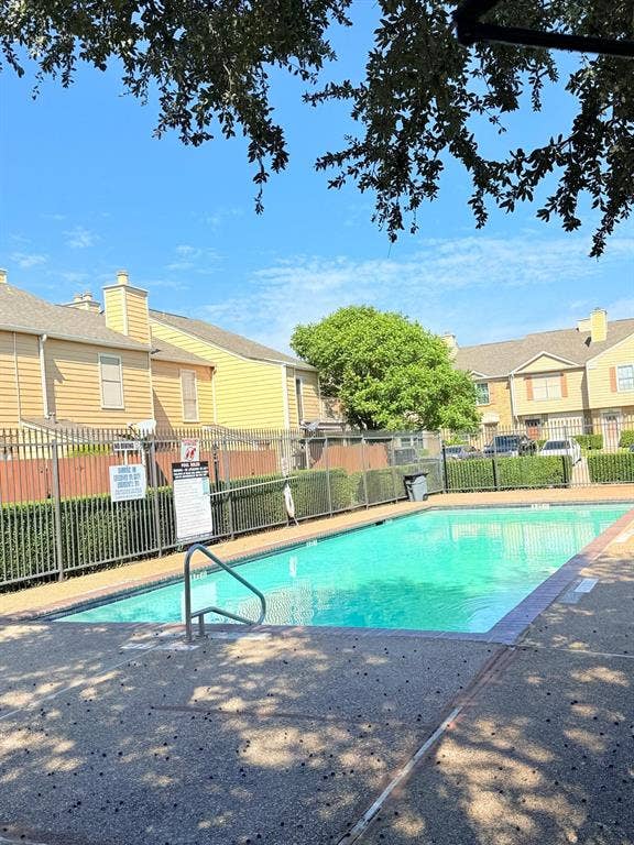 Swimming pool featuring a concrete deck, metal perimeter fencing, and stainless steel handrails