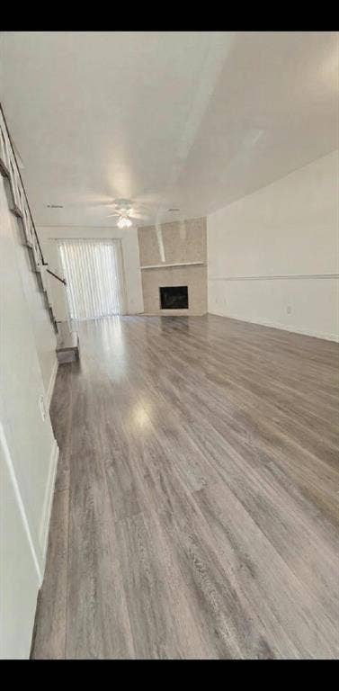 Living area featuring wood-finish flooring, a corner fireplace with a stone-finish surround, chair rail molding, and a ceiling fan
