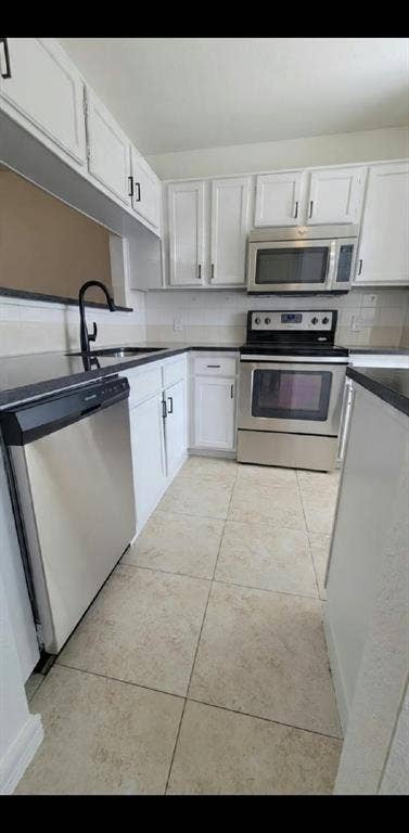 Kitchen featuring white cabinetry, dark countertops, tile flooring, stainless steel appliances, and a high-arch matte black faucet
