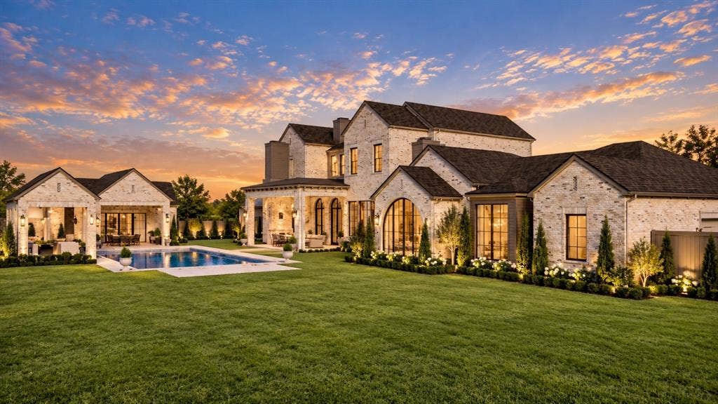 6002 Jericho Court, Dallas, TX 75248 Light-colored brick exterior featuring an expansive rear lawn, an in-ground swimming pool with stone surround, a covered patio with arched entries, and large multi-pane windows