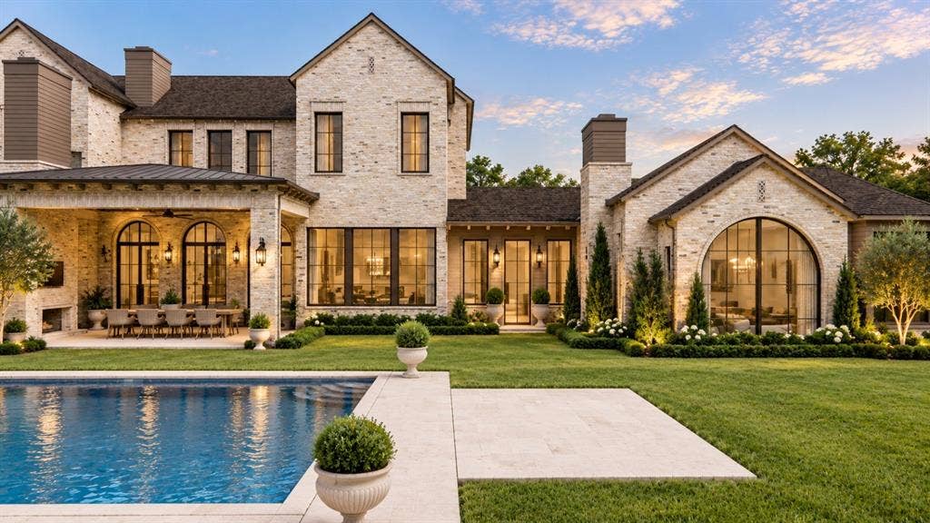 6002 Jericho Court, Dallas, TX 75248 Custom stone exterior featuring a covered patio, expansive swimming pool, large arched windows, and multi-gabled roofline