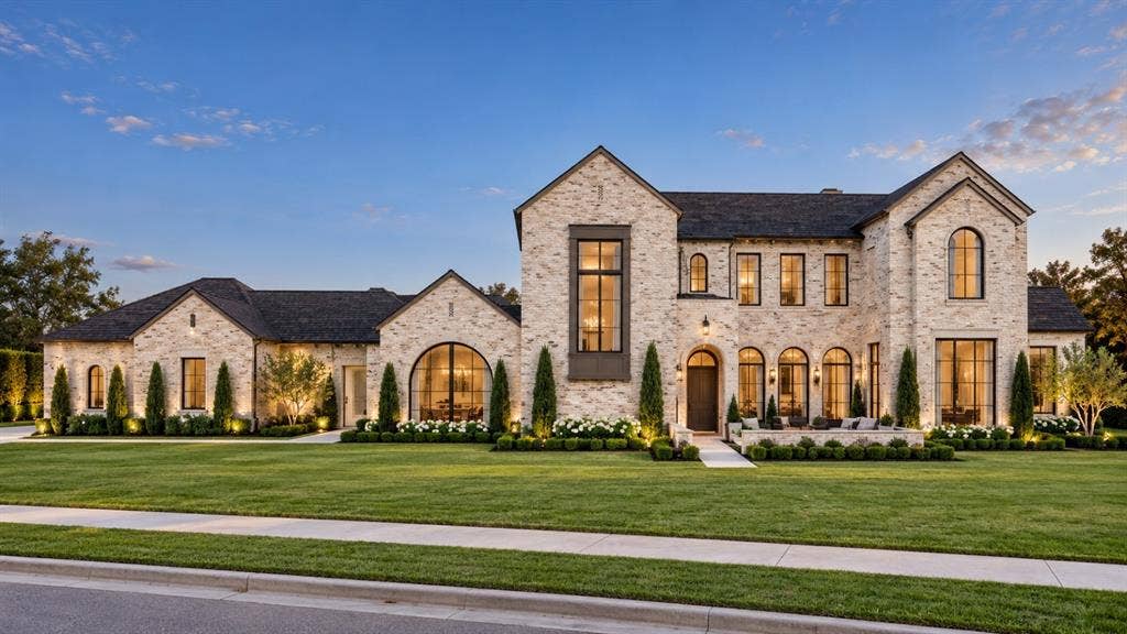 6002 Jericho Court, Dallas, TX 75248 Custom masonry exterior with light-toned brick, arched window detailing, steeply pitched gabled rooflines, large-format metal-framed windows, and manicured front lawn landscaping