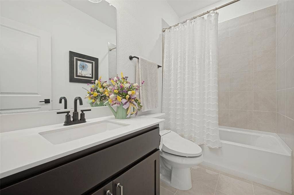 3417 Paintbrush Path, Melissa, TX 75454 Dark-toned vanity with a rectangular sink, crisp white countertop, matte black faucet, and a tub-shower combination featuring neutral wall tiling