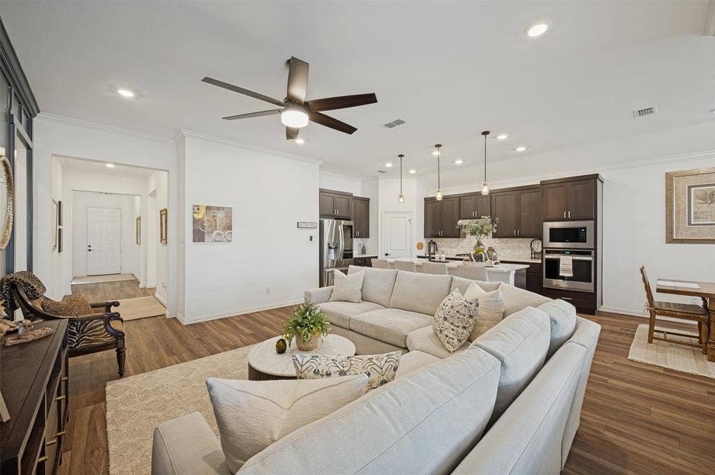 3417 Paintbrush Path, Melissa, TX 75454 Open-concept interior featuring wood-finish flooring, recessed ceiling lighting, a contemporary multi-blade ceiling fan, and a kitchen equipped with dark cabinetry, stone countertops, and built-in stainless steel appliances