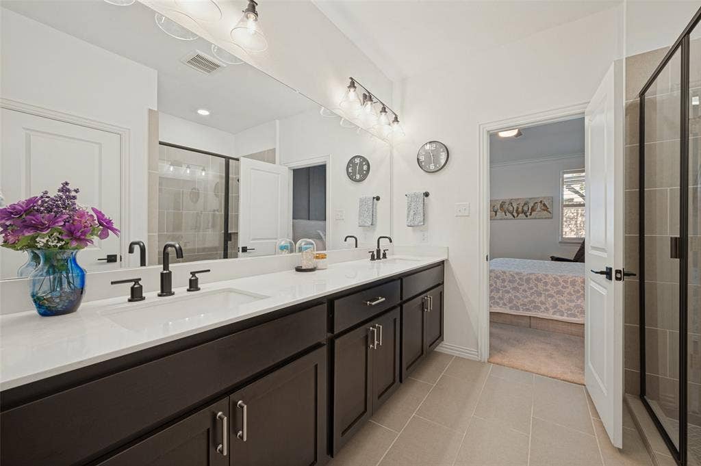3417 Paintbrush Path, Melissa, TX 75454 Dual-sink vanity with matte black fixtures, crisp white countertop, expansive wall-to-wall mirror, and glass-enclosed shower with neutral-toned tiling