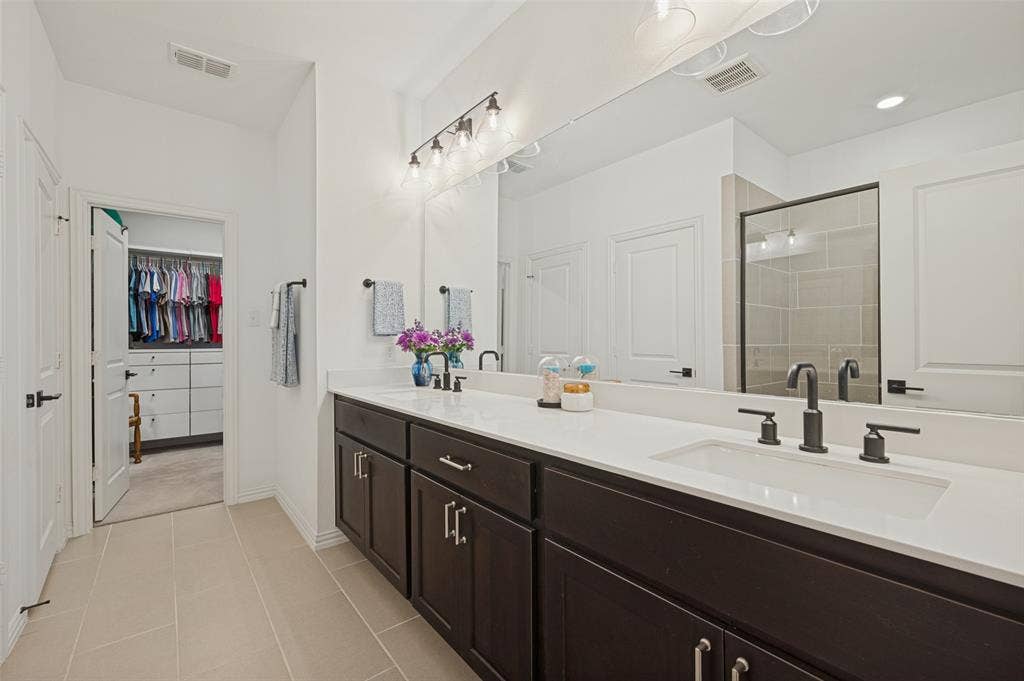 3417 Paintbrush Path, Melissa, TX 75454 Double vanity featuring dark cabinetry, solid-surface white countertops, rectangular undermount sinks, matte black widespread faucets, and a full-width mirror