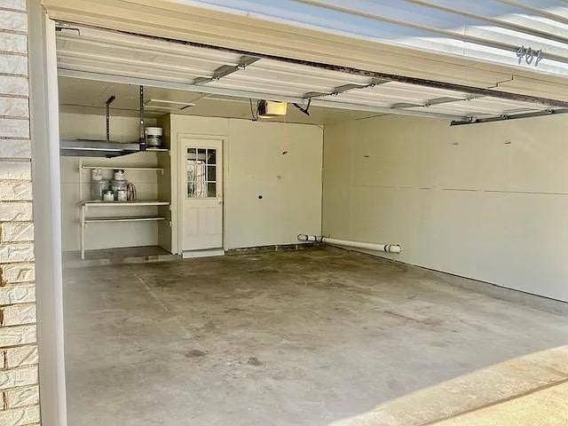 407 Cambridge Drive, Richardson, TX 75080 Two-car garage featuring a concrete floor, built-in shelving, overhead door mechanism, and a separate entry door with a windowed panel
