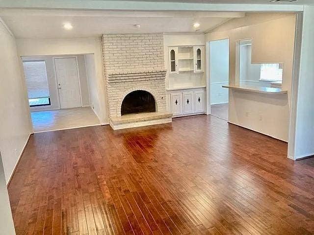 407 Cambridge Drive, Richardson, TX 75080 Living area featuring wood-finish flooring, a painted brick fireplace with an arched firebox, and built-in cabinetry with glass-front display shelving