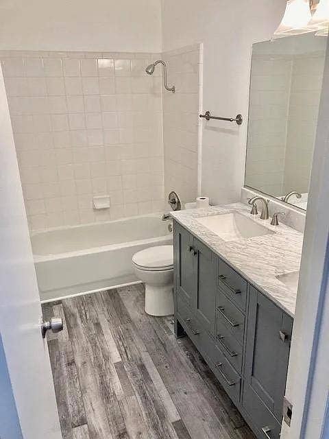 407 Cambridge Drive, Richardson, TX 75080 Grey shaker-style vanity with stone-finish countertop, dual-basin under-mount sinks, wood-finish flooring, and white tiled tub surround