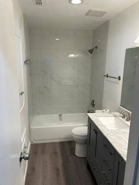 407 Cambridge Drive, Richardson, TX 75080 Bathroom featuring wood-finish flooring, a charcoal gray vanity with a light-toned countertop, and a tub-shower combination finished with large-format tile surround