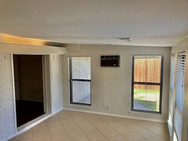 407 Cambridge Drive, Richardson, TX 75080 Interior room featuring tile flooring, painted brick wall accents, multiple windows with blinds, and a built-in window air conditioning unit