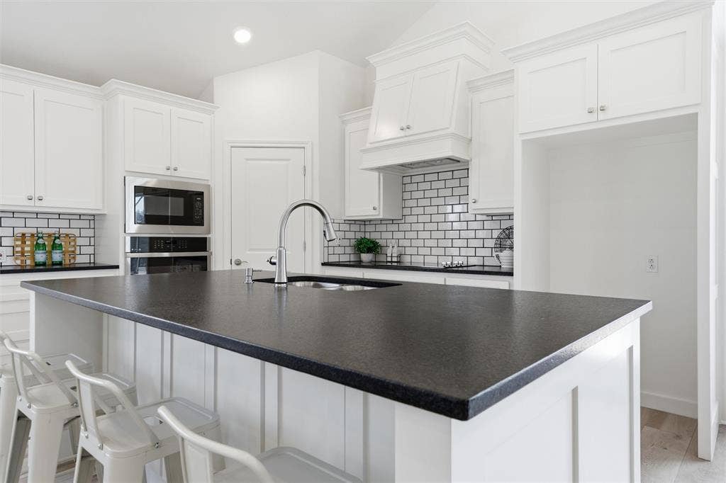 2303 Pilgrim Lane, Lorena, TX 76655 Kitchen featuring a central island with dark solid surface countertops, white cabinetry with crown molding, subway tile backsplash, and a built-in microwave and wall oven