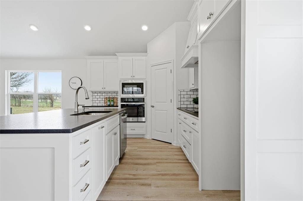 2303 Pilgrim Lane, Lorena, TX 76655 Kitchen featuring white shaker-style cabinetry, dark stone countertops, stainless steel wall-mounted oven and microwave, subway tile backsplash, and wood-finish flooring