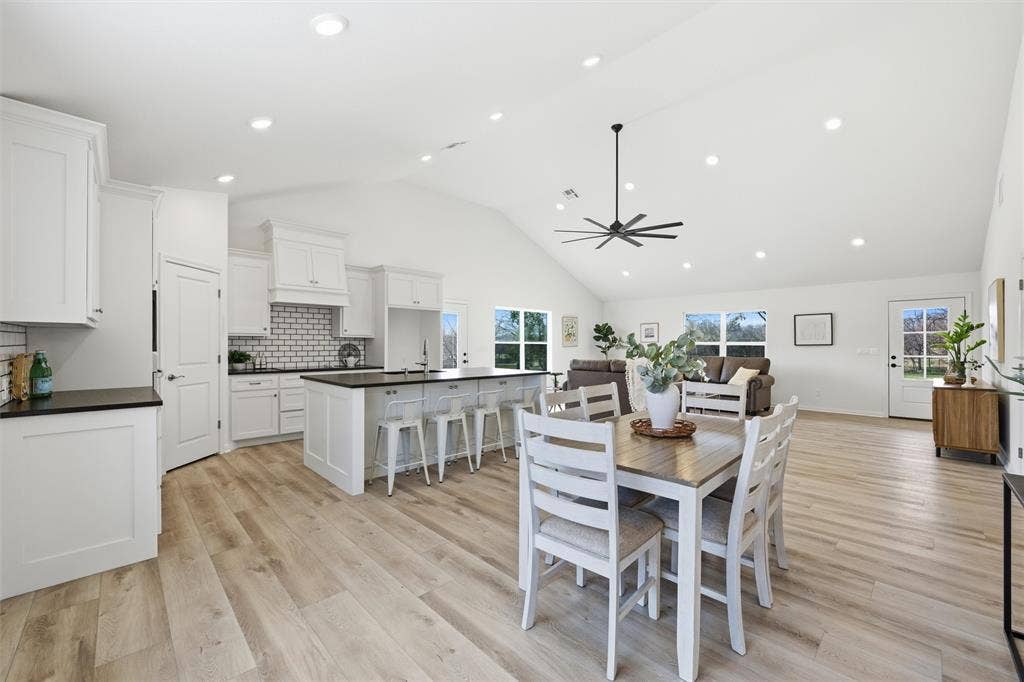 2303 Pilgrim Lane, Lorena, TX 76655 Open-concept kitchen and living area featuring vaulted ceilings, recessed lighting, wood-finish flooring, a central island with countertop seating, and a subway tile backsplash