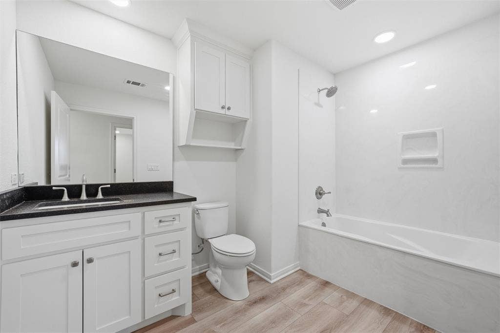 2303 Pilgrim Lane, Lorena, TX 76655 Bathroom featuring white cabinetry, dark stone countertop, integrated sink, wood-finish flooring, and a tub-shower combination with an inset wall niche