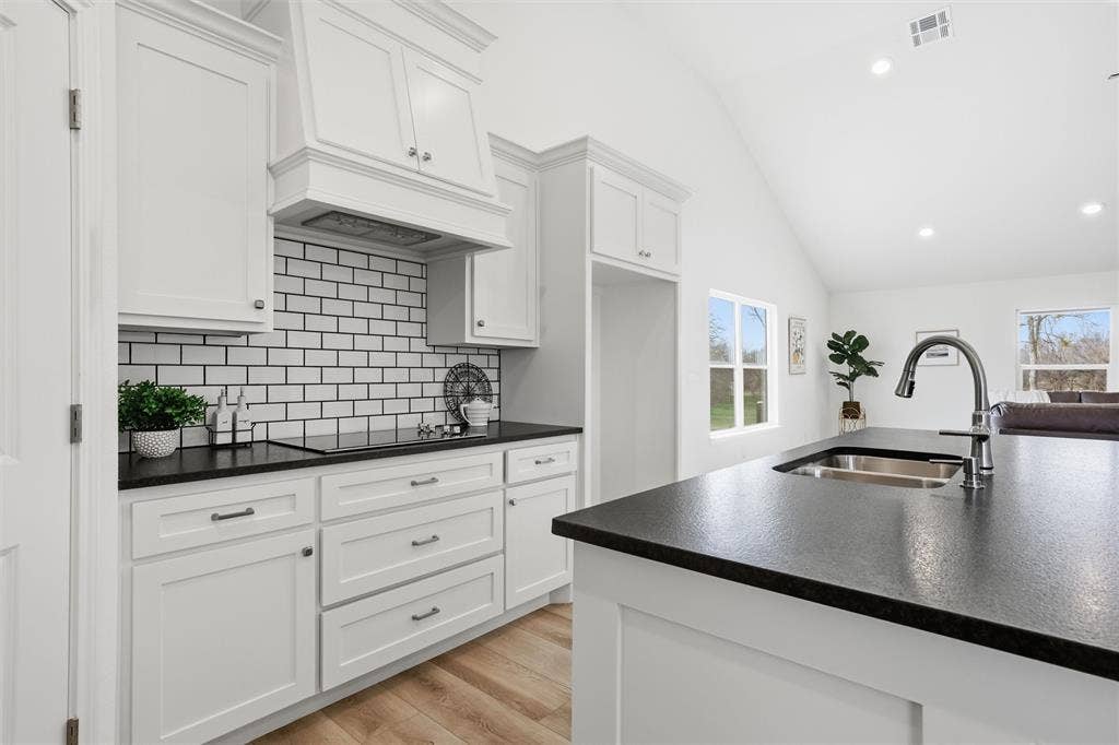 2303 Pilgrim Lane, Lorena, TX 76655 Kitchen featuring white shaker-style cabinetry, a contrasting dark countertop, subway tile backsplash, vaulted ceilings, and a central island with an undermount sink
