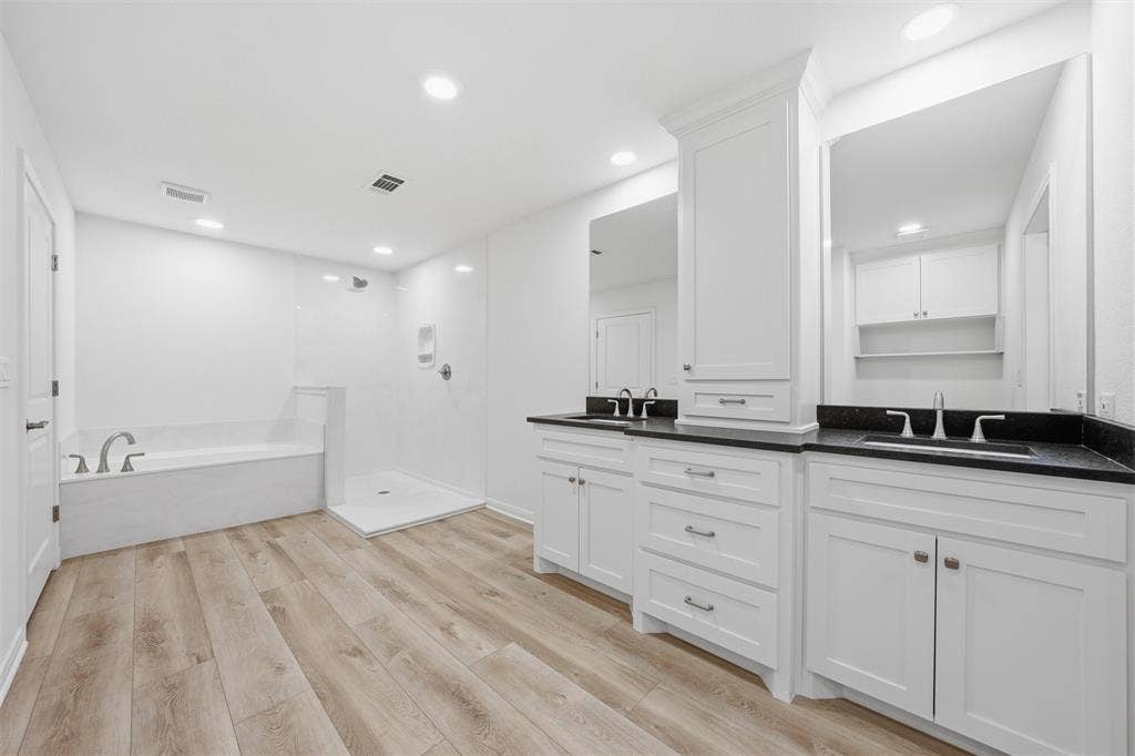 2303 Pilgrim Lane, Lorena, TX 76655 Dual vanity with white cabinetry and dark countertops, wood-finish flooring, built-in storage tower, soaking tub, and walk-in shower
