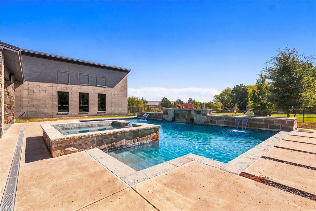 211 Hunter Pass, Waxahachie, TX 75165 In-ground swimming pool featuring a stacked-stone spa, cascading water features, and expansive concrete hardscaping