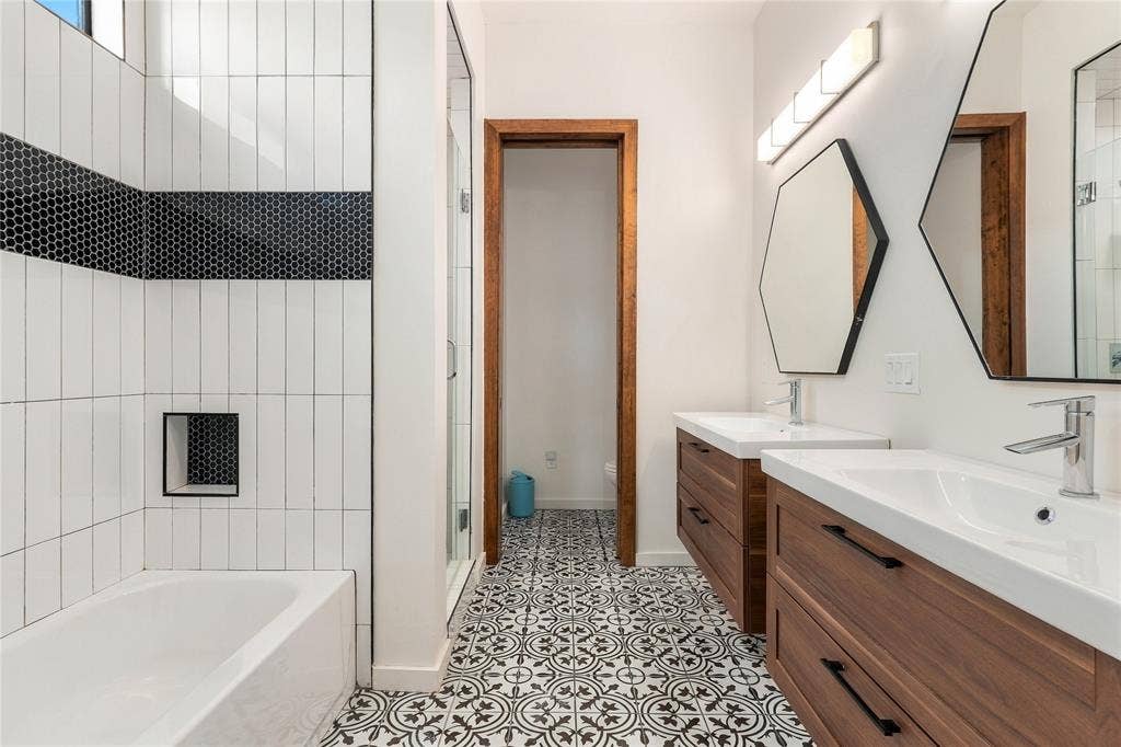 211 Hunter Pass, Waxahachie, TX 75165 Dual floating vanities with wood-finish cabinetry, patterned tile flooring, hexagonal wall mirrors, and a tiled shower surround with a built-in recessed niche