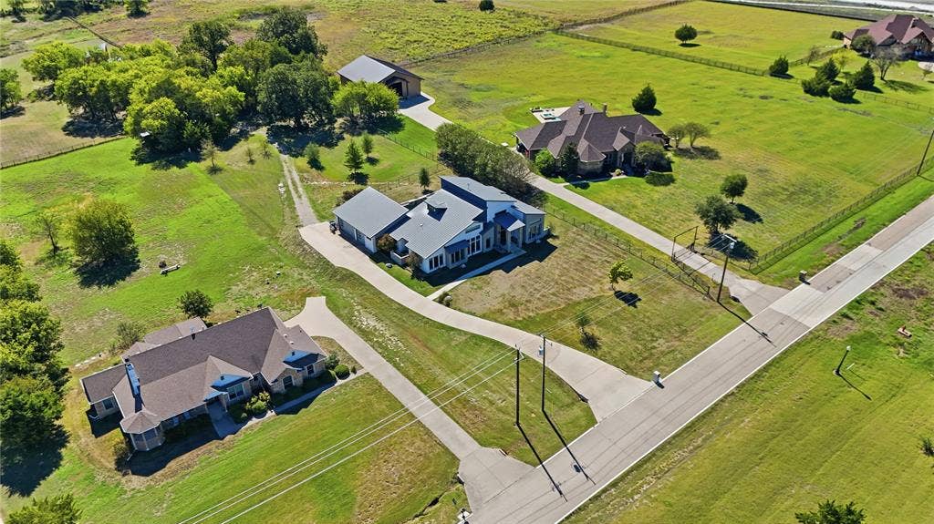 211 Hunter Pass, Waxahachie, TX 75165 Aerial perspective of a multi-structure property featuring expansive pasture land, multiple concrete driveways, a detached storage building, and fenced perimeter boundaries