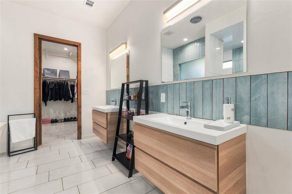 211 Hunter Pass, Waxahachie, TX 75165 Dual wall-mounted wooden vanities featuring white rectangular sinks, vertical blue ceramic tile backsplash, integrated lighting, and tile flooring