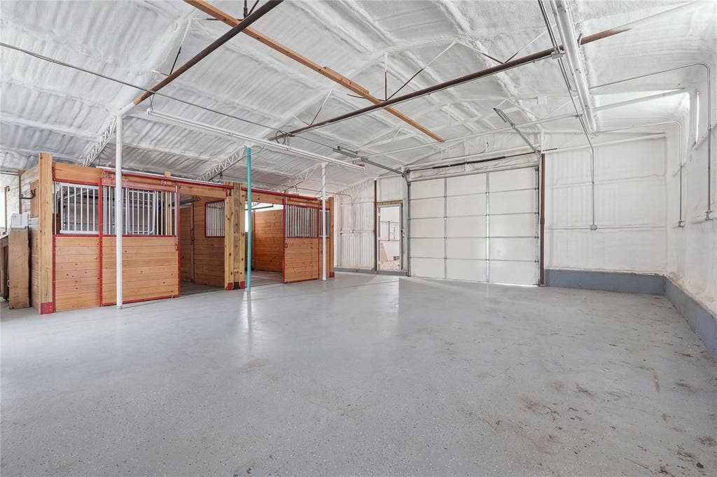 211 Hunter Pass, Waxahachie, TX 75165 Interior structure featuring sprayed foam insulation, wood-paneled stalls with metal grating, concrete flooring, and a large metal overhead door