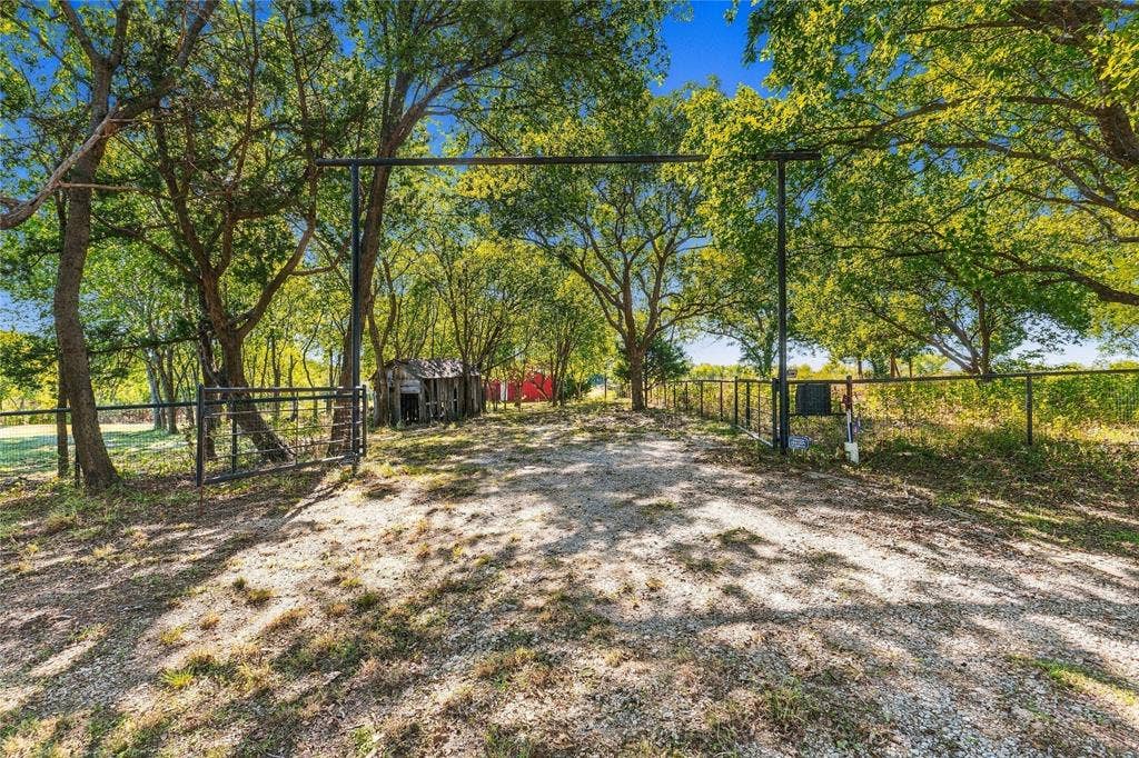 211 Hunter Pass, Waxahachie, TX 75165 Gravel driveway entrance featuring metal pipe fencing, a steel gate, and mature trees