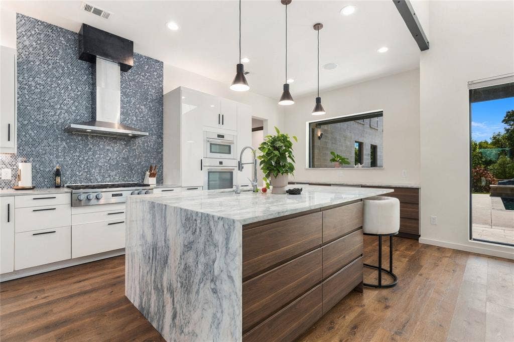 211 Hunter Pass, Waxahachie, TX 75165 Kitchen featuring a central island with a stone waterfall countertop, wood-finish cabinetry, built-in double wall ovens, stainless steel range hood, and textured mosaic tile backsplash