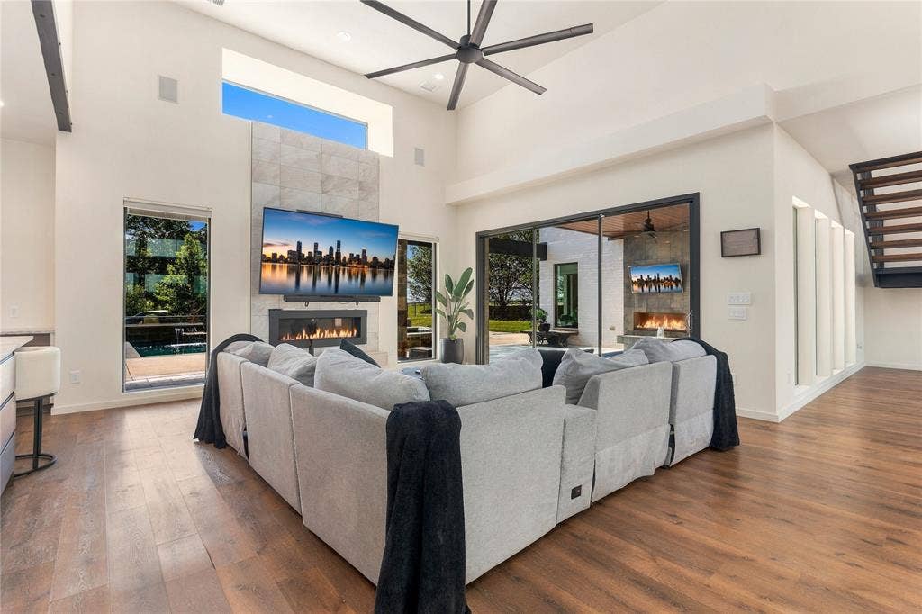 211 Hunter Pass, Waxahachie, TX 75165 Vaulted ceiling featuring a central multi-blade fan, stone-surround fireplace, large-format glass sliding doors, and wood-finish flooring