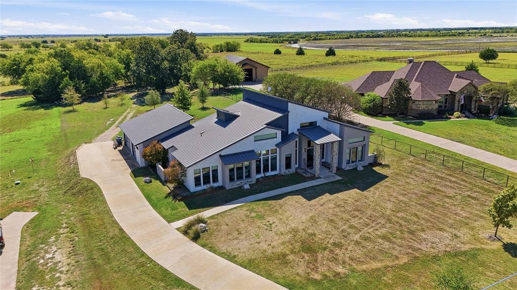 211 Hunter Pass, Waxahachie, TX 75165 Modern residence featuring a metal roof, clean-lined contemporary exterior, stone-accented entryway, attached garage, and expansive grounds