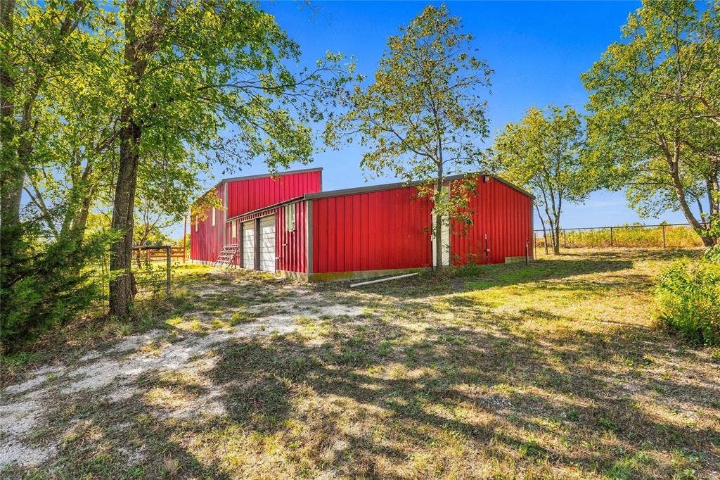 211 Hunter Pass, Waxahachie, TX 75165 Metal-sided red structure featuring dual garage doors, concrete foundation, and mature trees on a partially cleared lot