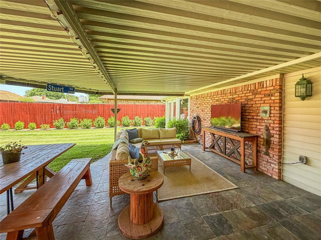 Covered patio with stamped concrete flooring, red brick accent wall, and perimeter fencing