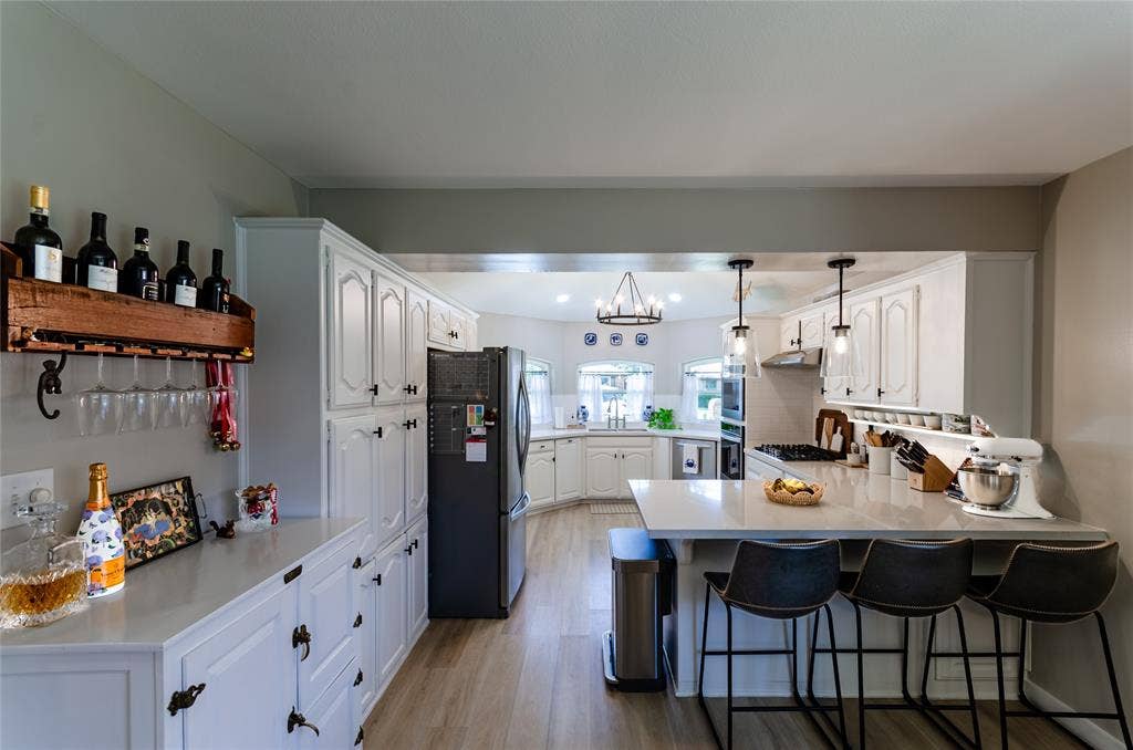 Wood-finish flooring, white cabinetry, integrated refrigerator, pendant lighting, and a kitchen island with seating