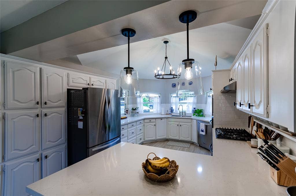 White cabinetry, stainless steel appliances, white subway tile backsplash, white countertops, and vaulted ceiling