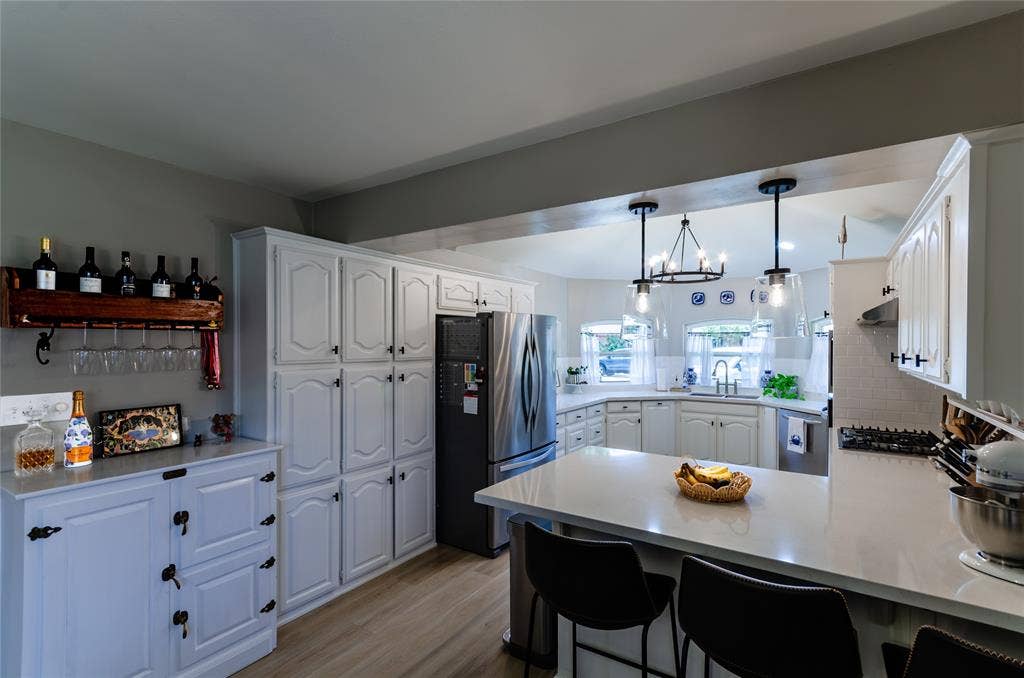 White cabinetry, wood-finish flooring, stainless steel appliances, white subway tile backsplash, and light-toned countertops