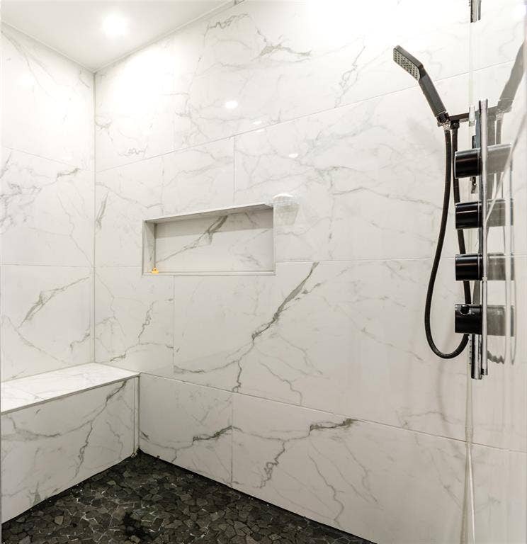Shower with marbled wall tile, built-in bench, recessed niche, and dark pebble floor tile