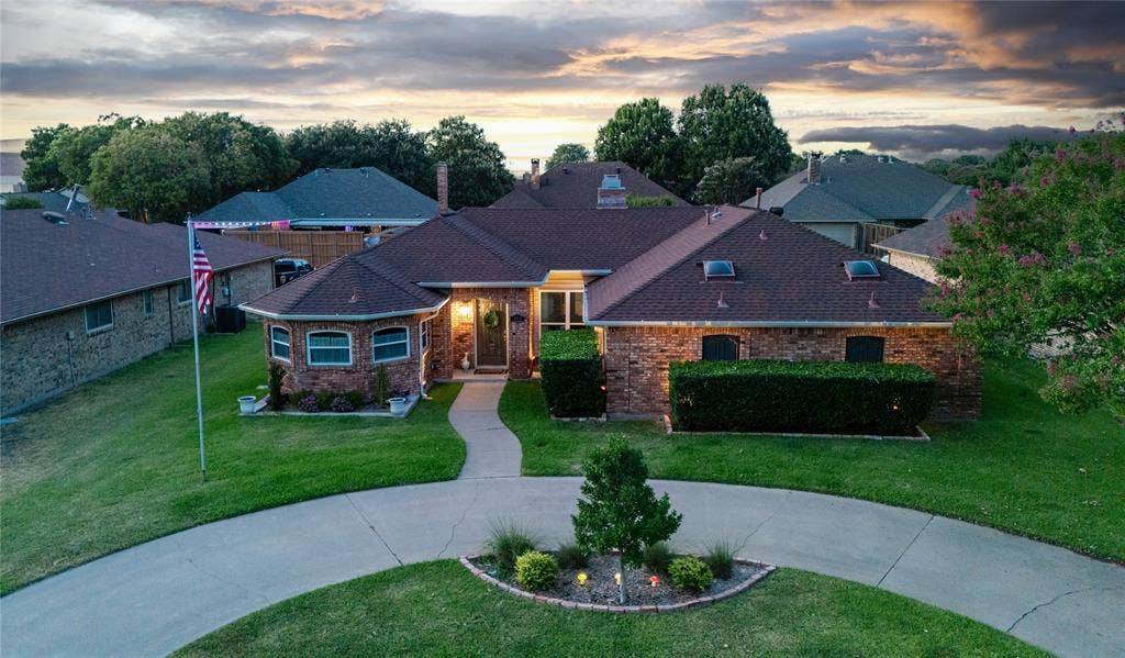 Brick exterior with a brown shingle roof, a circular driveway, a curved walkway, and landscaping