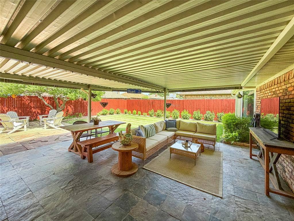 Expansive covered patio with slate-look flooring, exposed brick wall, and a manicured lawn