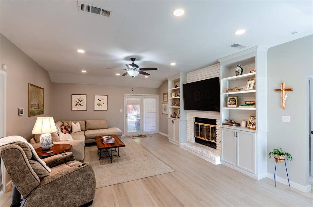 Recessed lighting, ceiling fan, wood-finish flooring, white brick fireplace, and built-in shelving with cabinetry