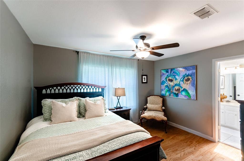 Wood-finish flooring, ceiling fan with integrated lighting, window with sheer curtains, and a doorway opening to an adjacent space