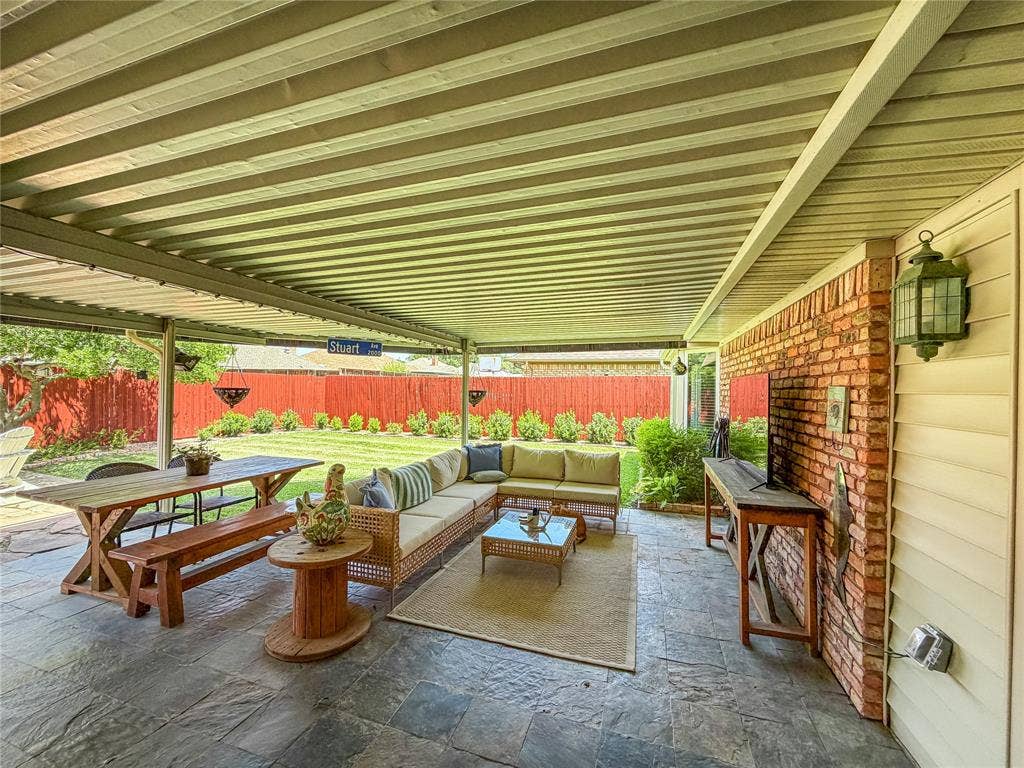 Covered patio with flagstone flooring, brick accent wall, and a manicured lawn