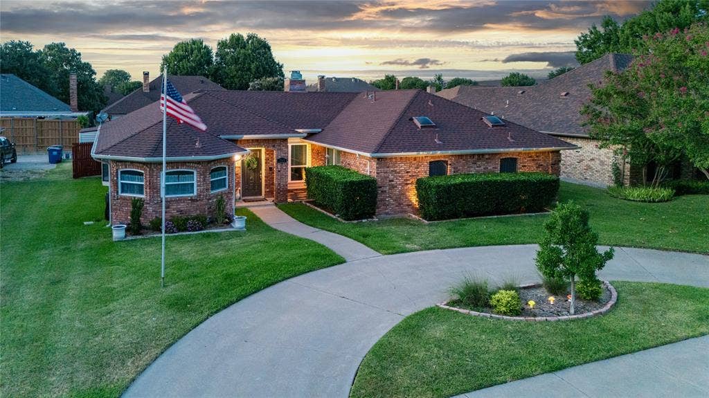 Brick exterior with a brown shingle roof, well-maintained lawn, skylights, and a curved driveway