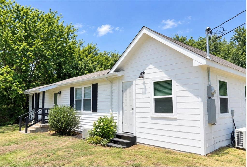 White horizontal lap siding exterior featuring black window shutters, a gabled roofline, and two metal-railed entry points