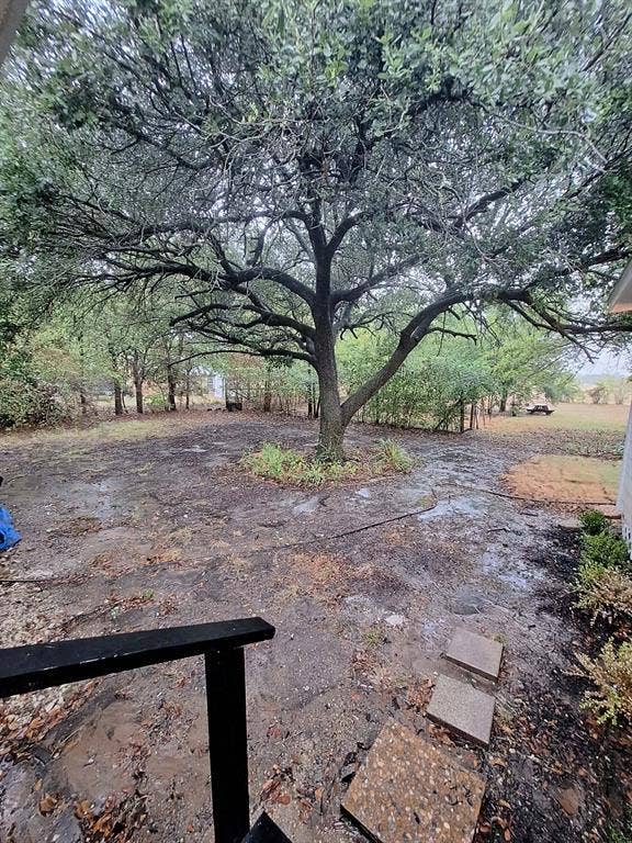 Expansive backyard featuring mature hardwood trees, natural stone patio, and perimeter fencing