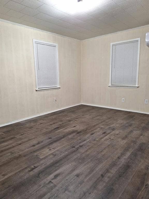 Room interior featuring wood-finish flooring, neutral wall paneling, dual windows with fitted blinds, and a tiled drop ceiling