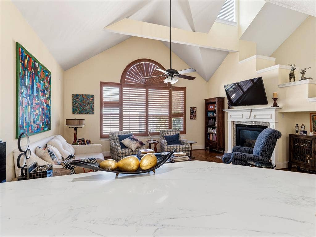 14567 Juliard Lane, Addison, TX 75001 Vaulted ceilings, fireplace with custom mantel, arched window with wood-finish shutters, and expansive stone-surface countertop