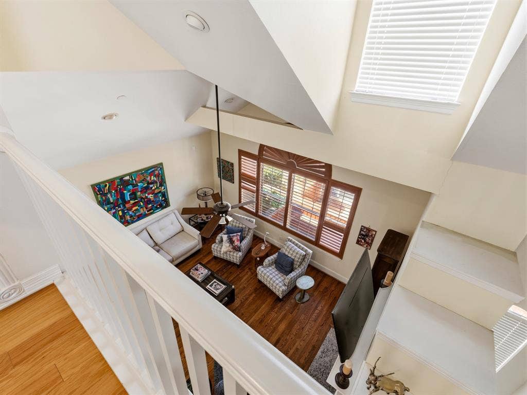 14567 Juliard Lane, Addison, TX 75001 Vaulted ceiling with overhead fan, expansive multi-pane windows with integrated shutters, wood-finish flooring, and white spindle staircase railing